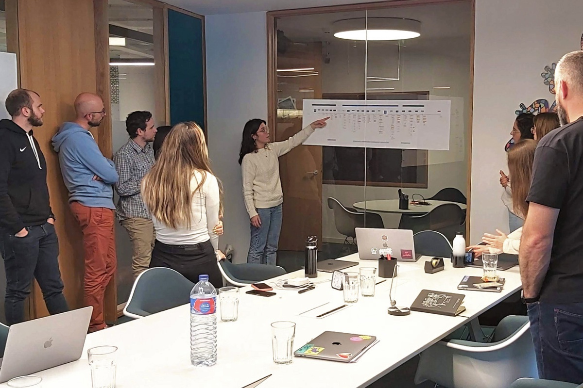 A woman present a UX journey map to a team of 4 other people watching.